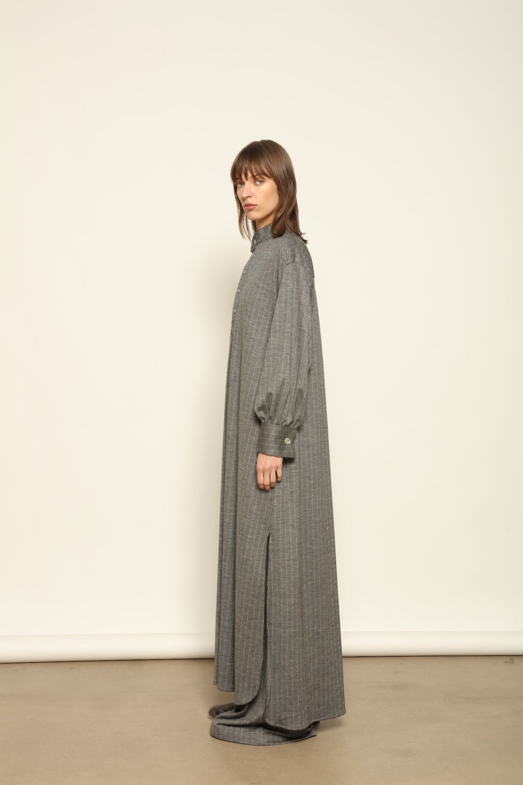 Model is wearing the Paul Dress by House of Woven Stories, made from sustainable wool with vertical stripes, a stand collar, and versatile styling for effortless elegance.