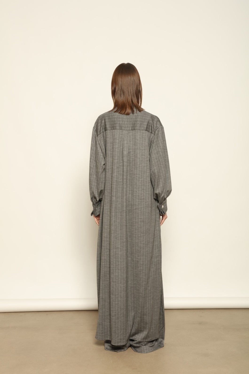 Model is wearing the Paul Dress by House of Woven Stories, made from sustainable wool with vertical stripes, a stand collar, and versatile styling for effortless elegance.