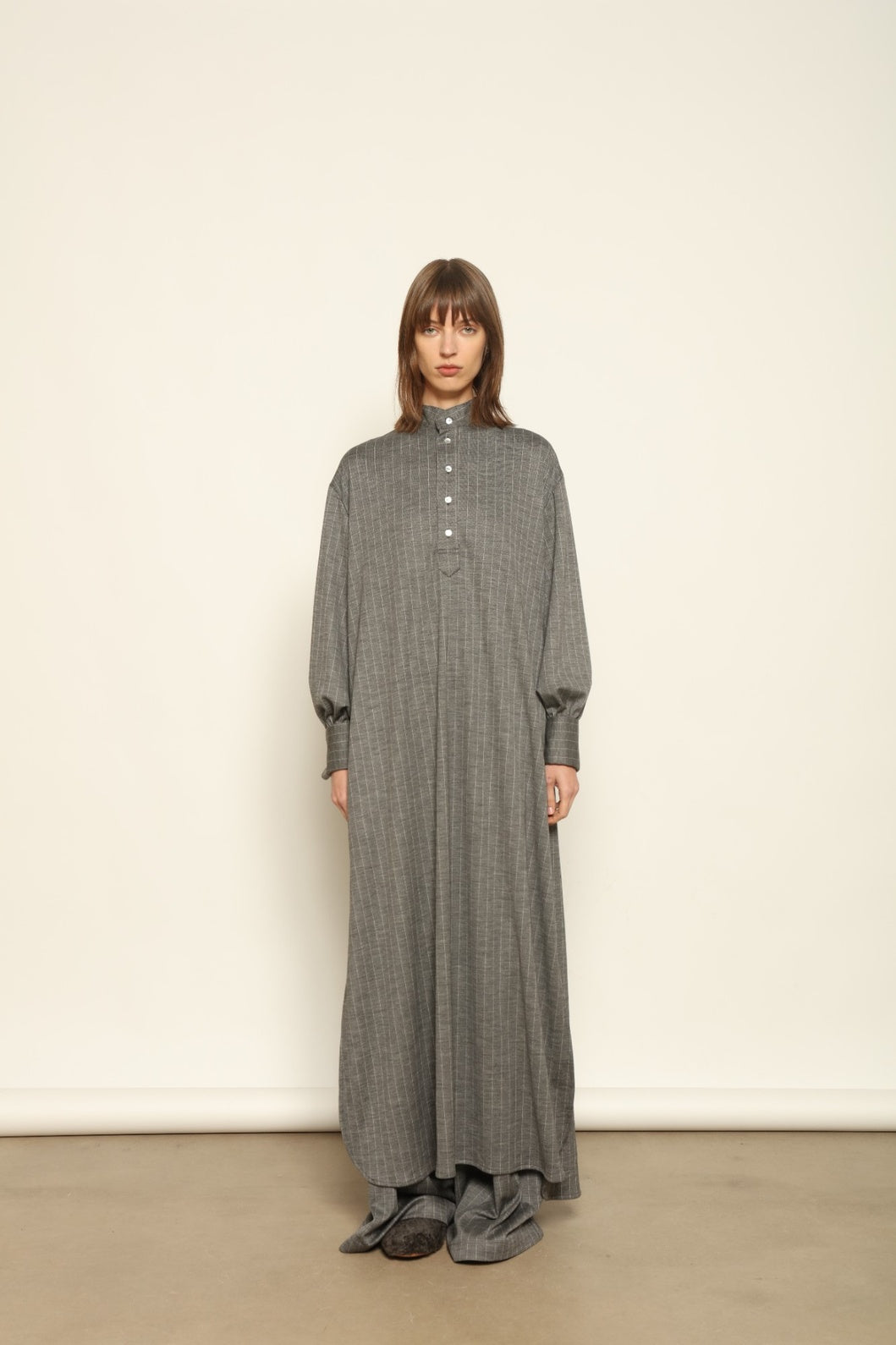 Model is wearing the Paul Dress by House of Woven Stories, made from sustainable wool with vertical stripes, a stand collar, and versatile styling for effortless elegance.