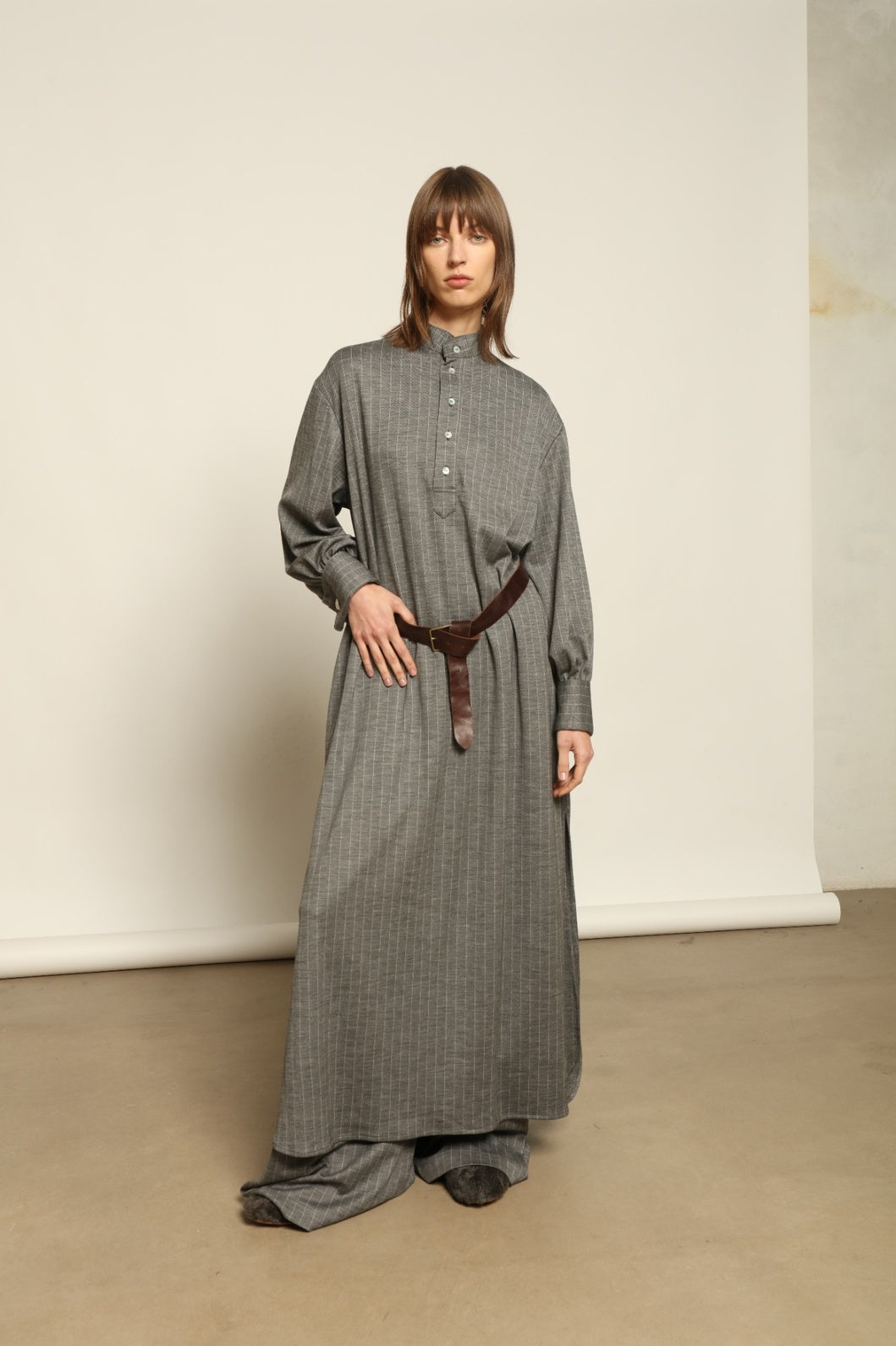 Model is wearing the Paul Dress by House of Woven Stories, made from sustainable wool with vertical stripes, a stand collar, and versatile styling for effortless elegance.