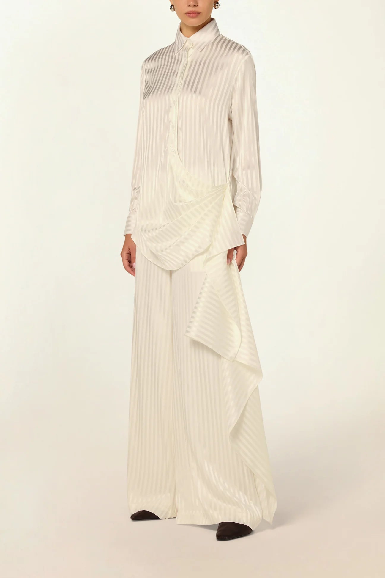 Elegant model wearing a luxury white striped silk blouse by Abadia with scarf drape detailing, featuring a fluid silhouette, classic collar, and refined minimalist styling.