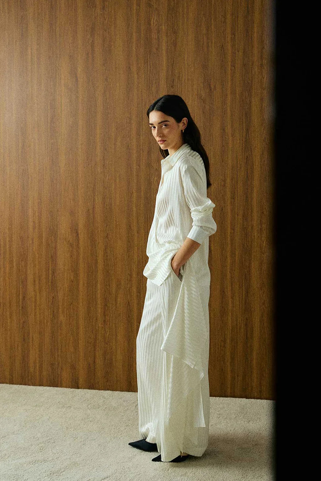 Elegant model wearing a luxury white striped silk blouse by Abadia with scarf drape detailing, featuring a fluid silhouette, classic collar, and refined minimalist styling.