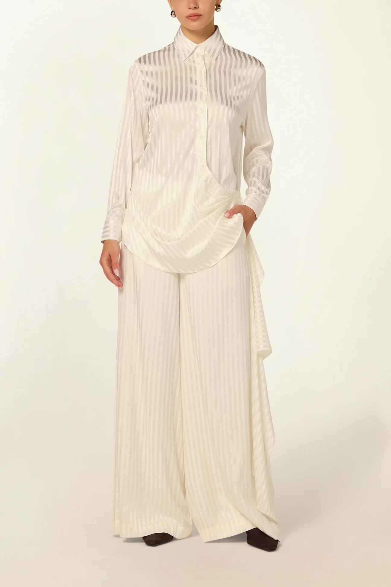 Elegant model wearing a luxury white striped silk blouse by Abadia with scarf drape detailing, featuring a fluid silhouette, classic collar, and refined minimalist styling.