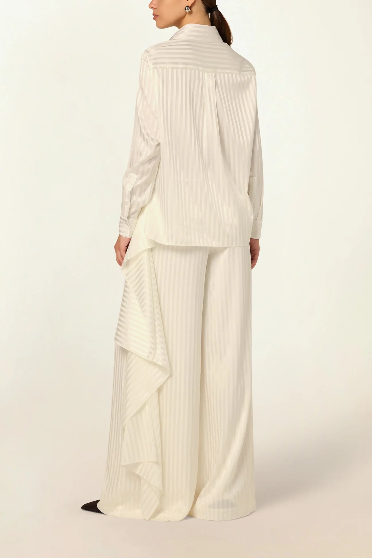 Elegant model wearing a luxury white striped silk blouse by Abadia with scarf drape detailing, featuring a fluid silhouette, classic collar, and refined minimalist styling.