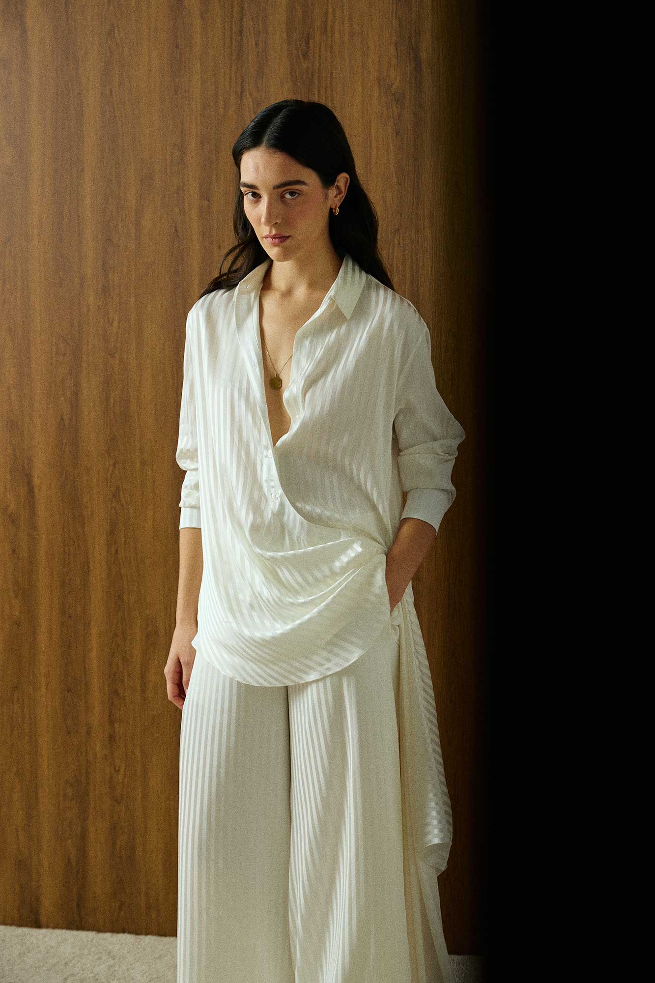 Elegant model wearing a luxury white striped silk blouse by Abadia with scarf drape detailing, featuring a fluid silhouette, classic collar, and refined minimalist styling.
