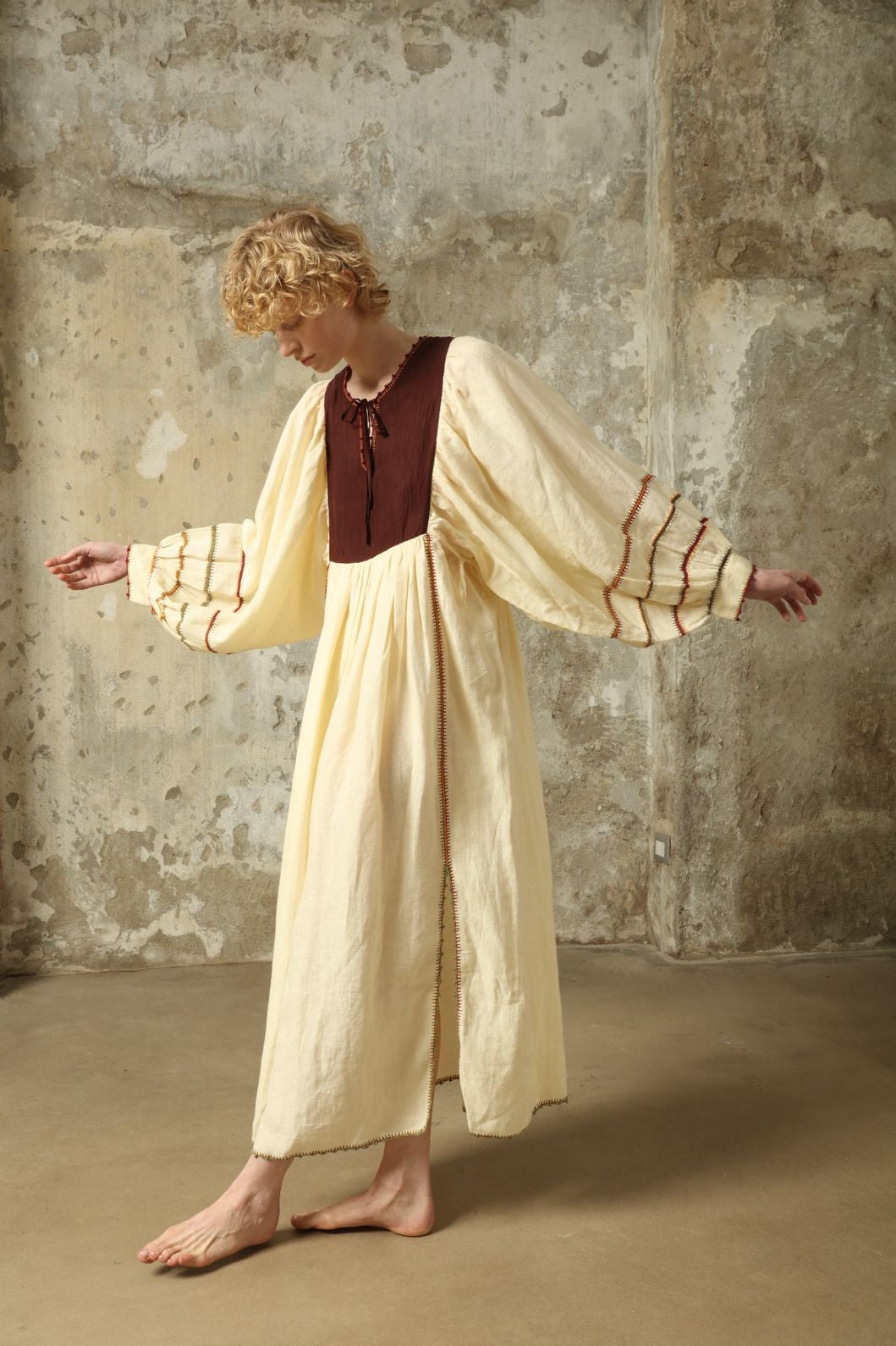 Model is wearing the Serafina Brown Linen Dress by Supernaturae x HONS, crafted in a blend of crisp linen and hand-spun silk with rich earthy botanical dye tones. Featuring a 1970s-inspired kaftan silhouette, hand-crochet edges and adjustable ties, this sustainable slow fashion piece shows natural tonal variations unique to each garment. Made in small-batch production in Mexico using ancestral techniques, part of the House of Woven Stories selection.