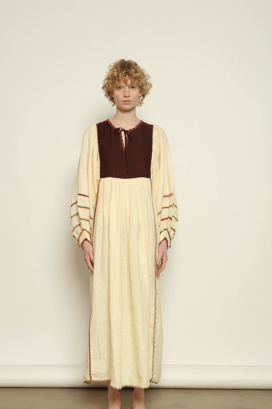 Model is wearing the Serafina Brown Linen Dress by Supernaturae x HONS, crafted in a blend of crisp linen and hand-spun silk with rich earthy botanical dye tones. Featuring a 1970s-inspired kaftan silhouette, hand-crochet edges and adjustable ties, this sustainable slow fashion piece shows natural tonal variations unique to each garment. Made in small-batch production in Mexico using ancestral techniques, part of the House of Woven Stories selection.