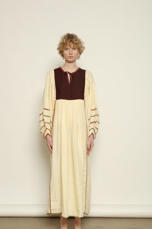 Model is wearing the Serafina Brown Linen Dress by Supernaturae x HONS, crafted in a blend of crisp linen and hand-spun silk with rich earthy botanical dye tones. Featuring a 1970s-inspired kaftan silhouette, hand-crochet edges and adjustable ties, this sustainable slow fashion piece shows natural tonal variations unique to each garment. Made in small-batch production in Mexico using ancestral techniques, part of the House of Woven Stories selection.