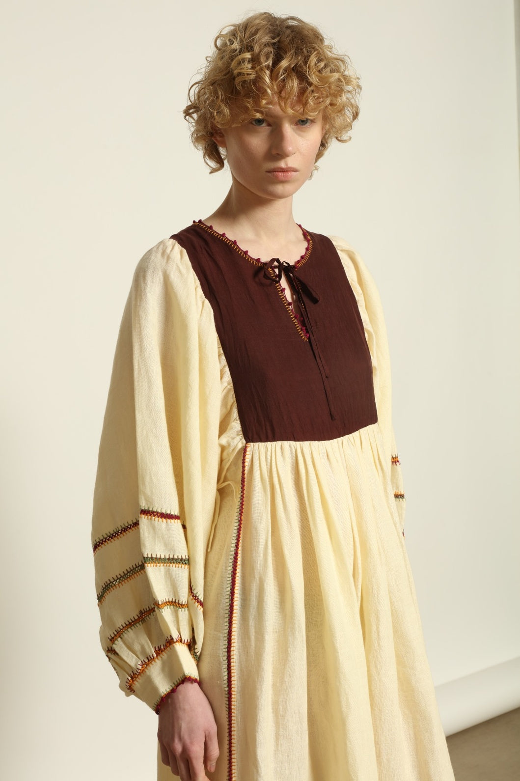 Model is wearing the Serafina Brown Linen Dress by Supernaturae x HONS, crafted in a blend of crisp linen and hand-spun silk with rich earthy botanical dye tones. Featuring a 1970s-inspired kaftan silhouette, hand-crochet edges and adjustable ties, this sustainable slow fashion piece shows natural tonal variations unique to each garment. Made in small-batch production in Mexico using ancestral techniques, part of the House of Woven Stories selection.