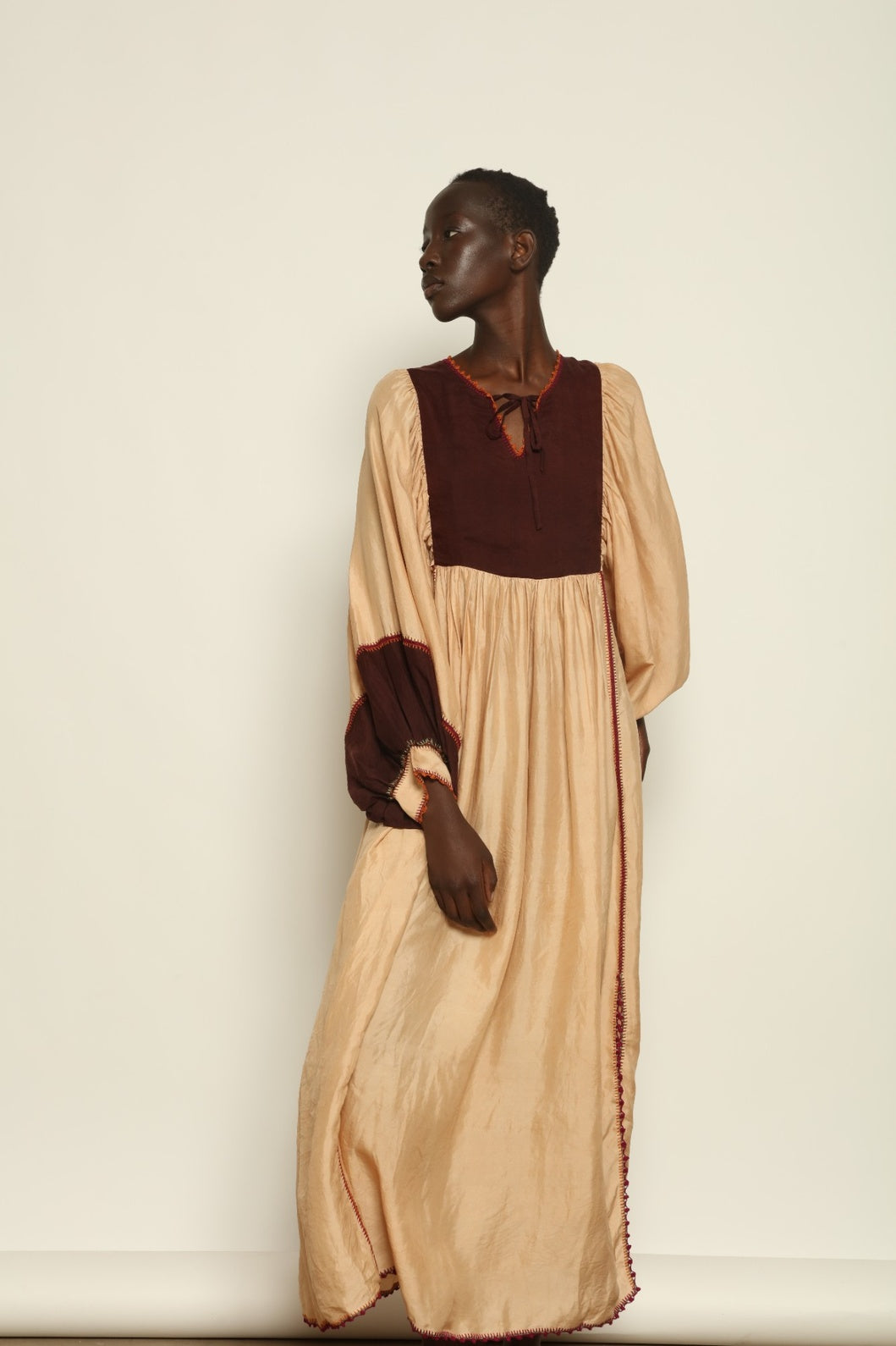 Model is wearing the Serafina Cream and Brown Silk Dress by Supernaturae x HONS, crafted in ethereal silk chiffon with cream and earthy brown botanical dyes. Featuring a 1970s-inspired flowing silhouette and delicate hand-crochet details, this sustainable slow luxury dress shows natural organic pattern variations created by plant-based pigments. Made in collaboration with artisan communities in Mexico, part of the House of Woven Stories selection