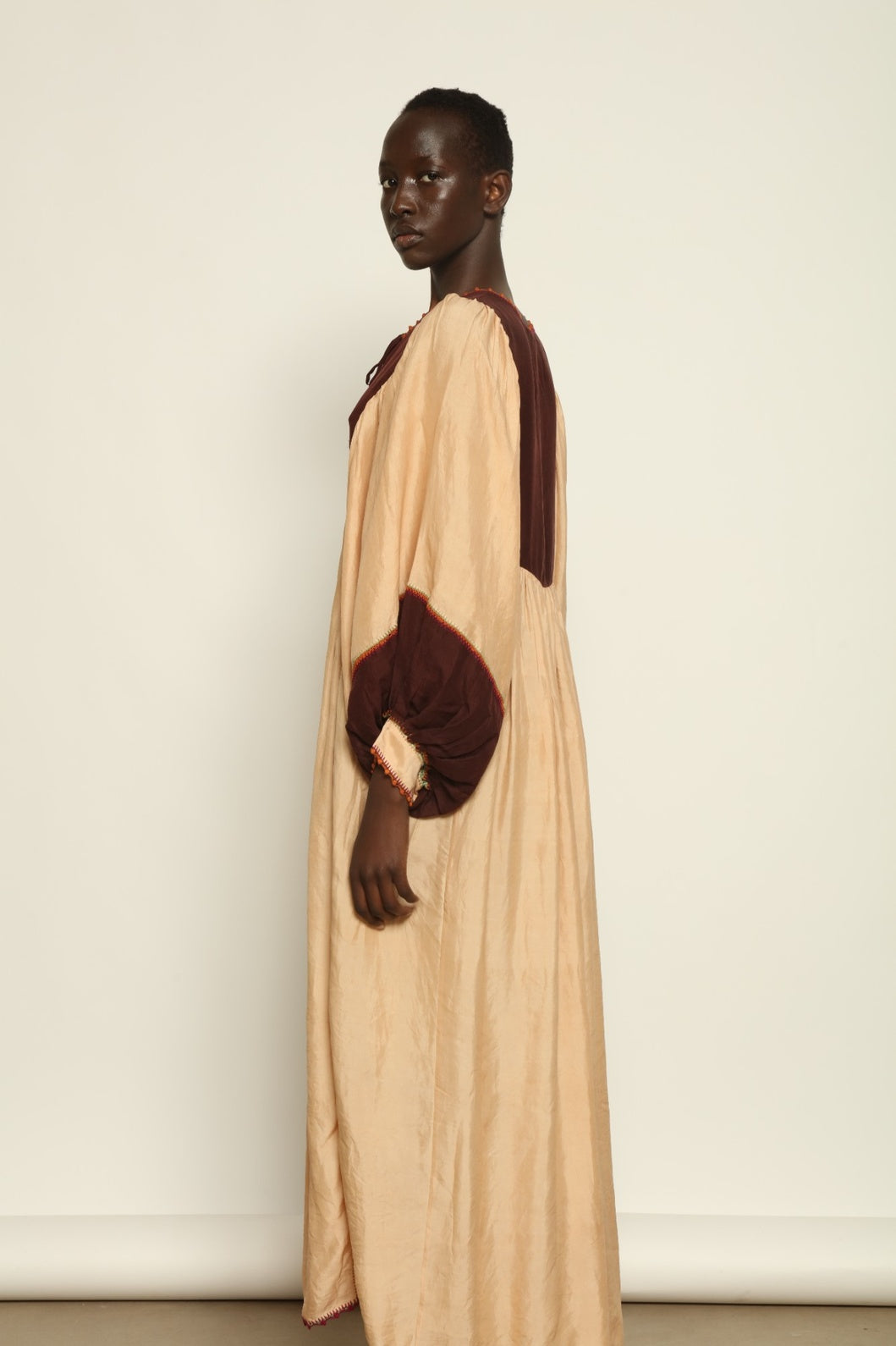 Model is wearing the Serafina Cream and Brown Silk Dress by Supernaturae x HONS, crafted in ethereal silk chiffon with cream and earthy brown botanical dyes. Featuring a 1970s-inspired flowing silhouette and delicate hand-crochet details, this sustainable slow luxury dress shows natural organic pattern variations created by plant-based pigments. Made in collaboration with artisan communities in Mexico, part of the House of Woven Stories selection