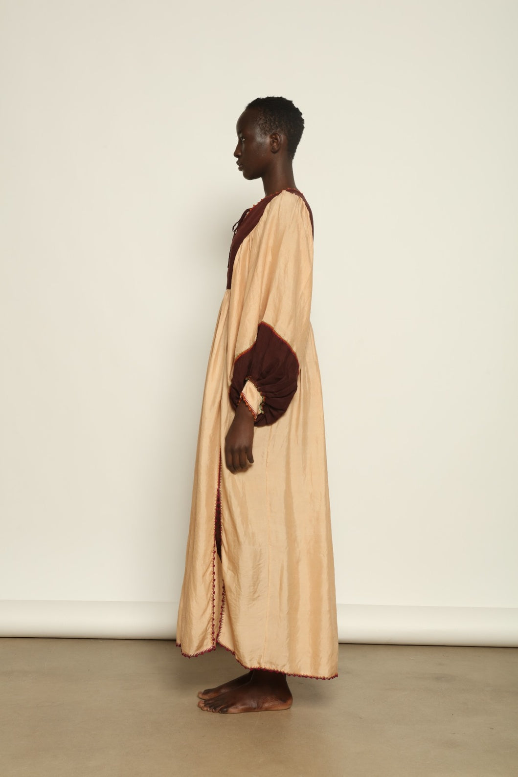 Model is wearing the Serafina Cream and Brown Silk Dress by Supernaturae x HONS, crafted in ethereal silk chiffon with cream and earthy brown botanical dyes. Featuring a 1970s-inspired flowing silhouette and delicate hand-crochet details, this sustainable slow luxury dress shows natural organic pattern variations created by plant-based pigments. Made in collaboration with artisan communities in Mexico, part of the House of Woven Stories selection