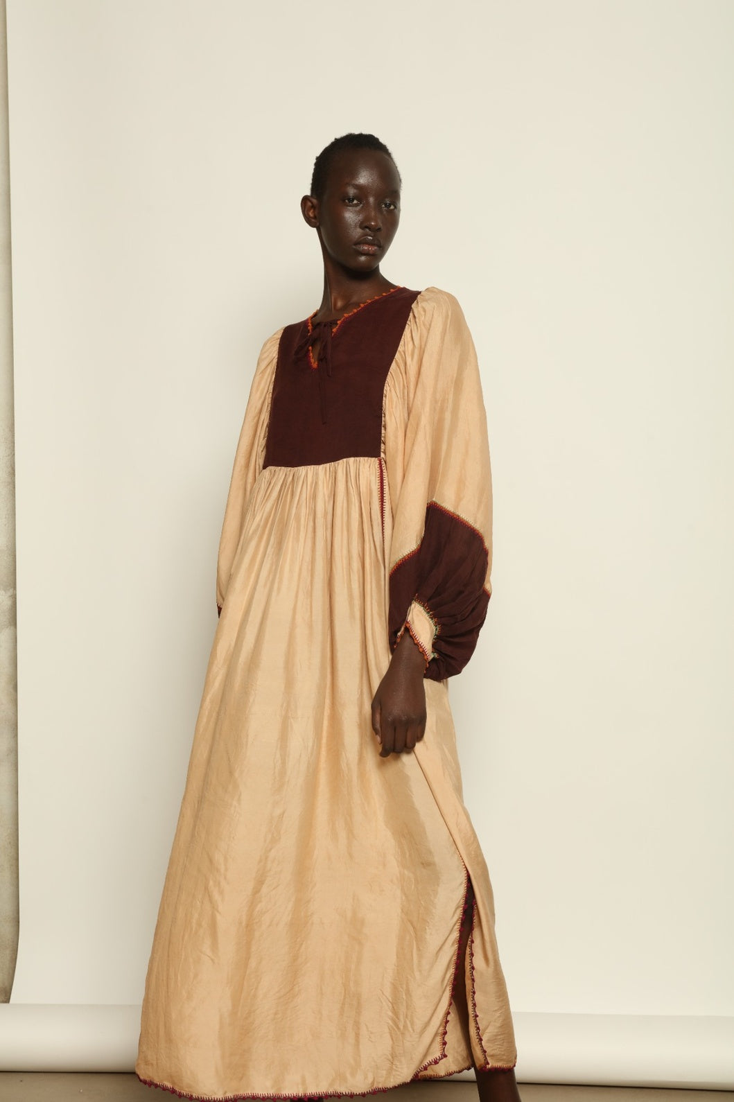 Model is wearing the Serafina Cream and Brown Silk Dress by Supernaturae x HONS, crafted in ethereal silk chiffon with cream and earthy brown botanical dyes. Featuring a 1970s-inspired flowing silhouette and delicate hand-crochet details, this sustainable slow luxury dress shows natural organic pattern variations created by plant-based pigments. Made in collaboration with artisan communities in Mexico, part of the House of Woven Stories selection