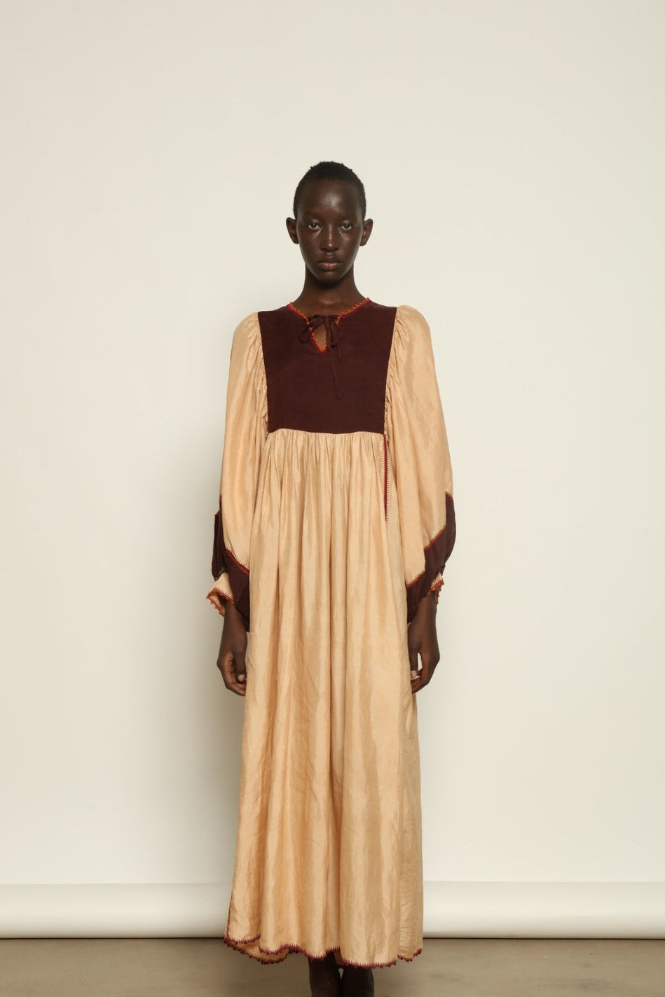 Model is wearing the Serafina Cream and Brown Silk Dress by Supernaturae x HONS, crafted in ethereal silk chiffon with cream and earthy brown botanical dyes. Featuring a 1970s-inspired flowing silhouette and delicate hand-crochet details, this sustainable slow luxury dress shows natural organic pattern variations created by plant-based pigments. Made in collaboration with artisan communities in Mexico, part of the House of Woven Stories selection
