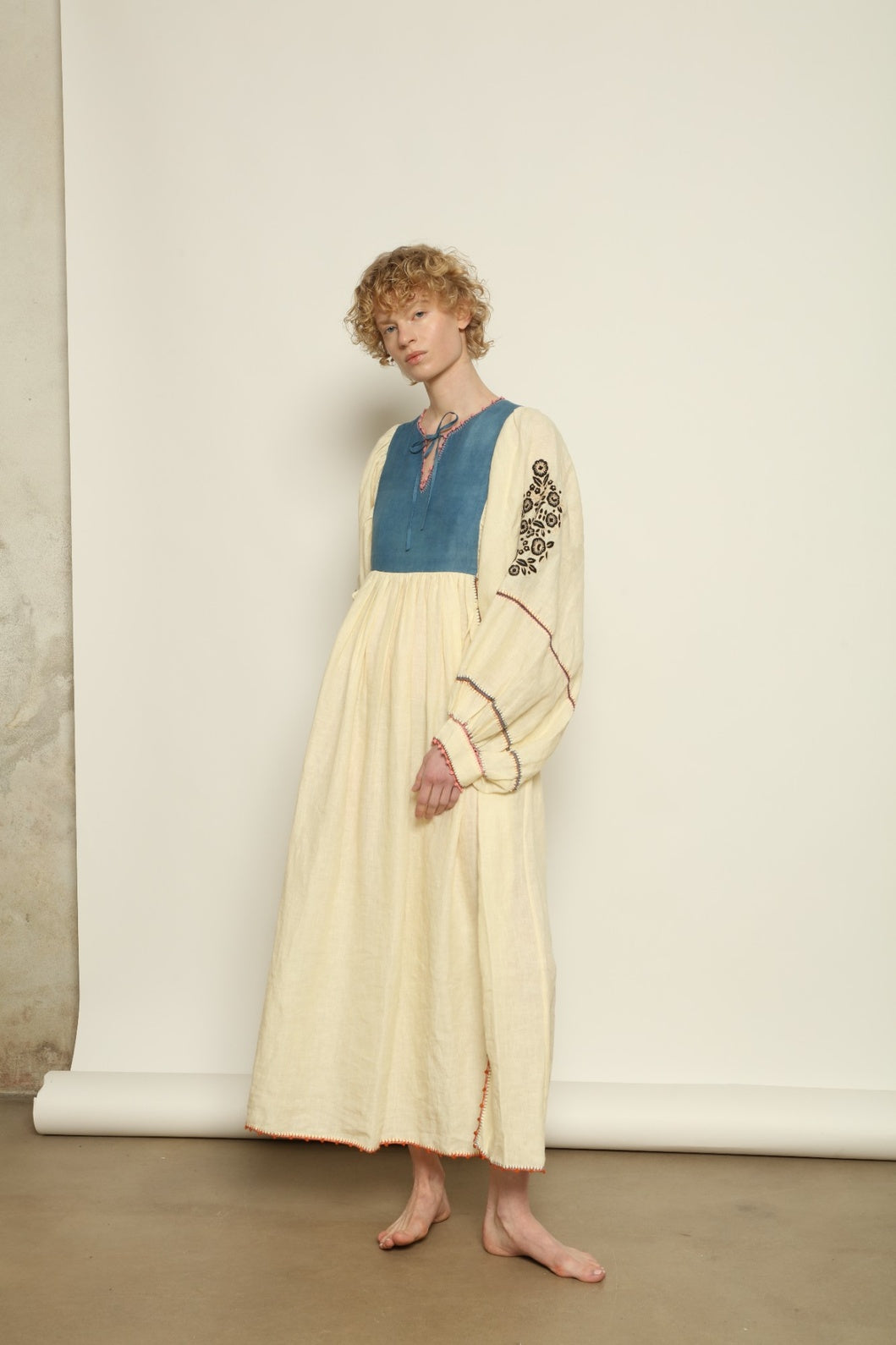 Model is wearing the Serafina Embroidered Blue Linen Dress by Supernaturae x HONS, crafted in a blend of crisp linen and hand-spun silk with deep natural indigo dye tones. This sustainable slow fashion piece features delicate hand embroidery and crochet edges, created through ancestral artisan techniques between India and Mexico. Part of the House of Nomad Stories selection.