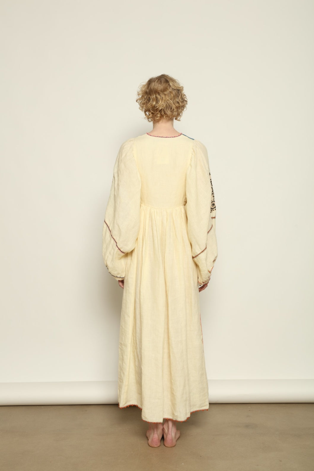 Model is wearing the Serafina Embroidered Blue Linen Dress by Supernaturae x HONS, crafted in a blend of crisp linen and hand-spun silk with deep natural indigo dye tones. This sustainable slow fashion piece features delicate hand embroidery and crochet edges, created through ancestral artisan techniques between India and Mexico. Part of the House of Nomad Stories selection.