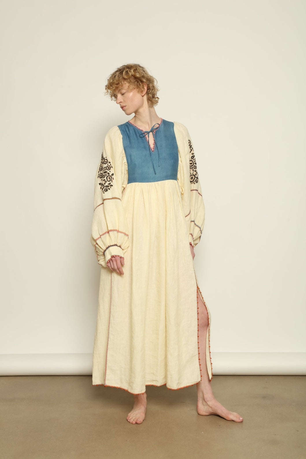 Model is wearing the Serafina Embroidered Blue Linen Dress by Supernaturae x HONS, crafted in a blend of crisp linen and hand-spun silk with deep natural indigo dye tones. This sustainable slow fashion piece features delicate hand embroidery and crochet edges, created through ancestral artisan techniques between India and Mexico. Part of the House of Nomad Stories selection.