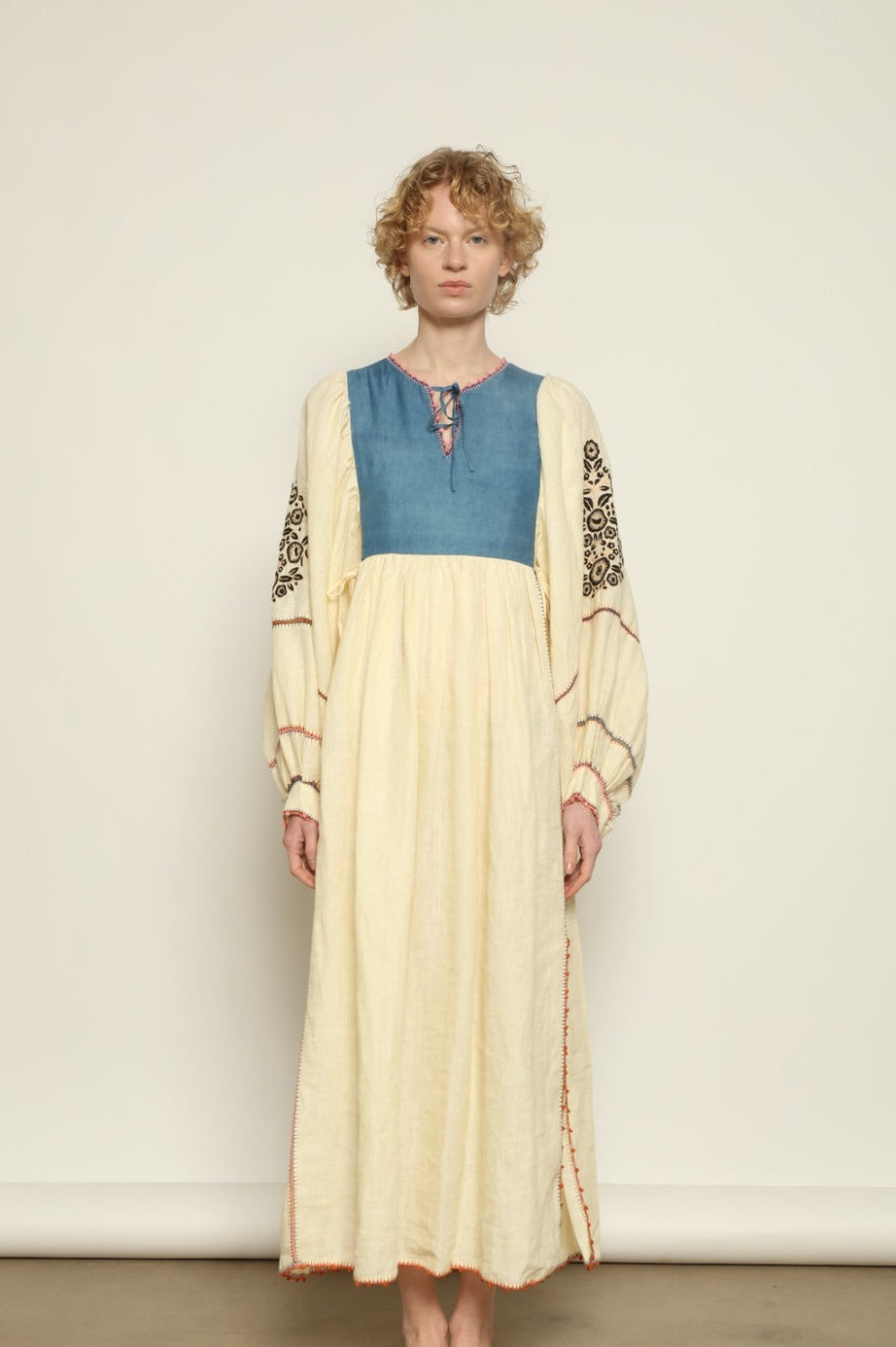 Model is wearing the Serafina Embroidered Blue Linen Dress by Supernaturae x HONS, crafted in a blend of crisp linen and hand-spun silk with deep natural indigo dye tones. This sustainable slow fashion piece features delicate hand embroidery and crochet edges, created through ancestral artisan techniques between India and Mexico. Part of the House of Nomad Stories selection.