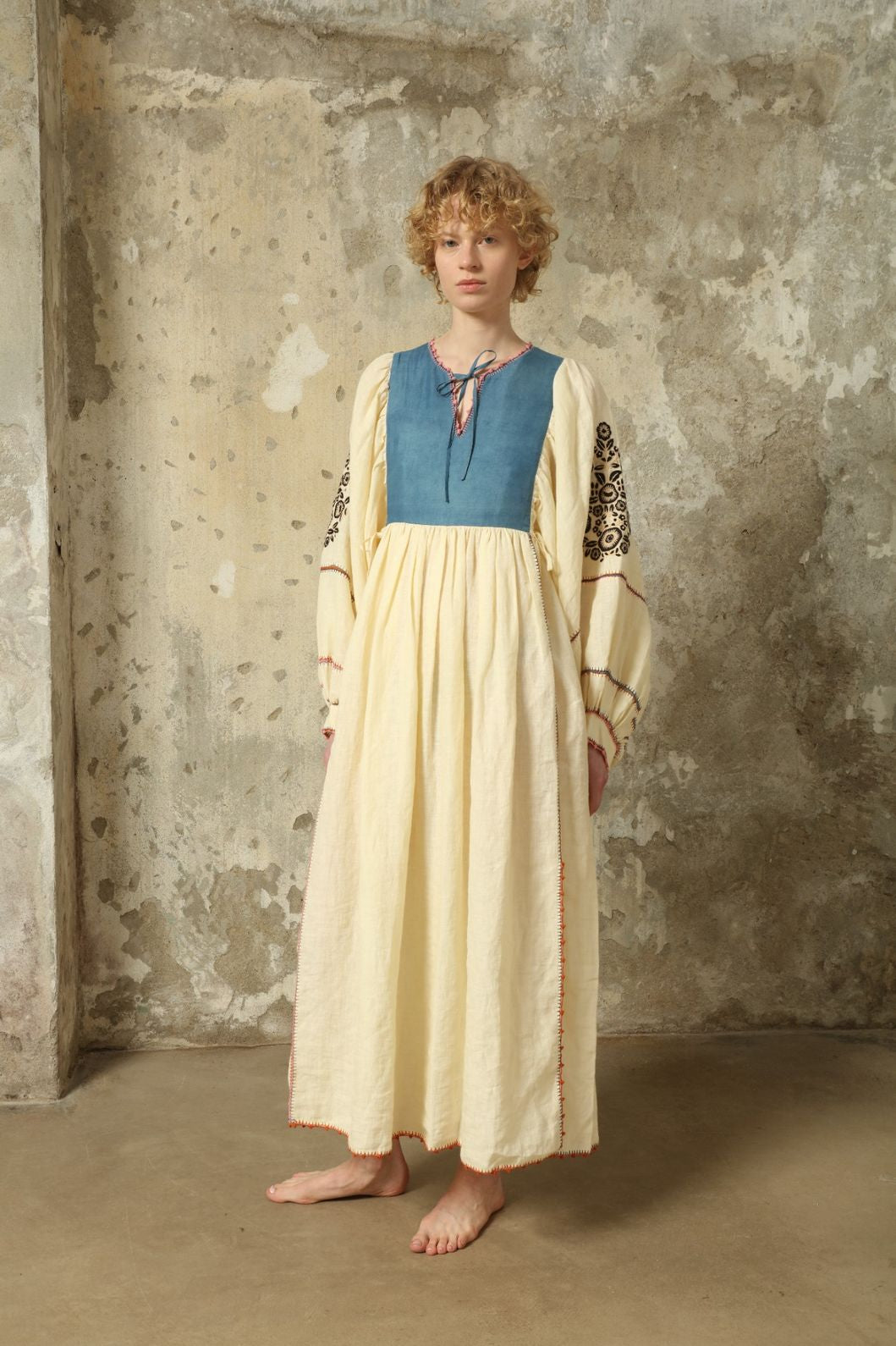 Model is wearing the Serafina Embroidered Blue Linen Dress by Supernaturae x HONS, crafted in a blend of crisp linen and hand-spun silk with deep natural indigo dye tones. This sustainable slow fashion piece features delicate hand embroidery and crochet edges, created through ancestral artisan techniques between India and Mexico. Part of the House of Nomad Stories selection.
