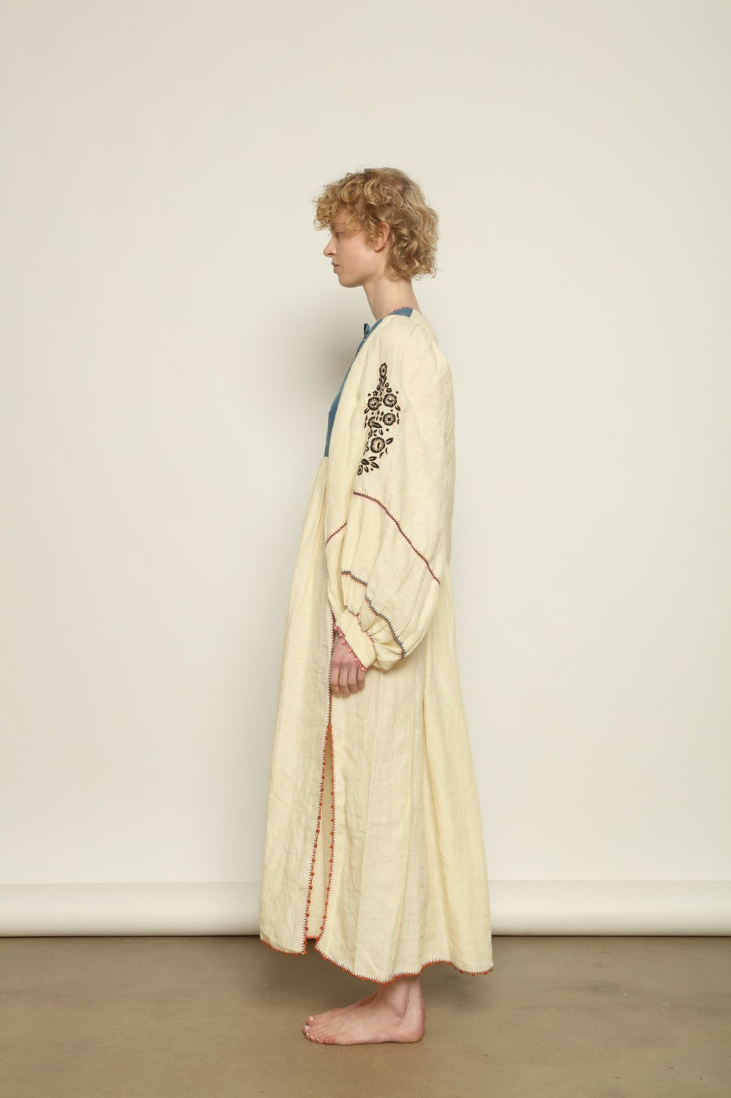Model is wearing the Serafina Embroidered Blue Linen Dress by Supernaturae x HONS, crafted in a blend of crisp linen and hand-spun silk with deep natural indigo dye tones. This sustainable slow fashion piece features delicate hand embroidery and crochet edges, created through ancestral artisan techniques between India and Mexico. Part of the House of Nomad Stories selection.