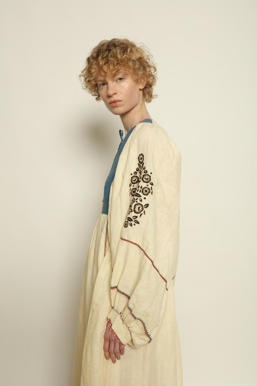 Model is wearing the Serafina Embroidered Blue Linen Dress by Supernaturae x HONS, crafted in a blend of crisp linen and hand-spun silk with deep natural indigo dye tones. This sustainable slow fashion piece features delicate hand embroidery and crochet edges, created through ancestral artisan techniques between India and Mexico. Part of the House of Nomad Stories selection.