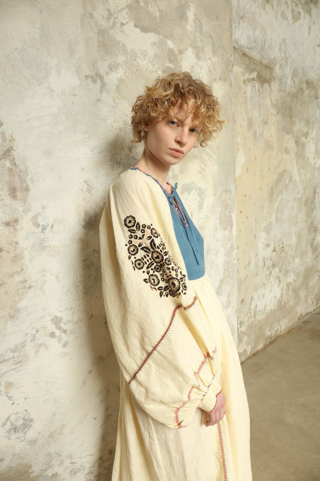 Model is wearing the Serafina Embroidered Blue Linen Dress by Supernaturae x HONS, crafted in a blend of crisp linen and hand-spun silk with deep natural indigo dye tones. This sustainable slow fashion piece features delicate hand embroidery and crochet edges, created through ancestral artisan techniques between India and Mexico. Part of the House of Nomad Stories selection.