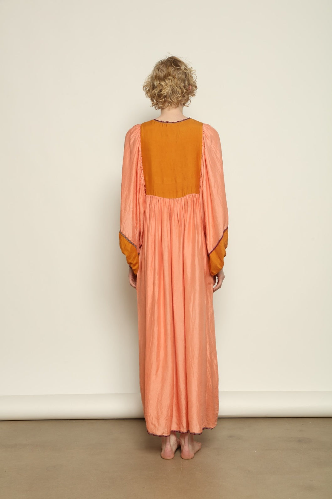 Model is wearing the Serafina Rose and Yellow Silk Dress by Supernaturae x HONS in pure handwoven silk, featuring a flowing kaftan-inspired silhouette with soft rose and golden yellow botanical-dyed tones. This sustainable artisan-made dress shows natural color variations unique to each piece, with lightweight breathable fabric and adjustable side ties, part of the House of Nomad Stories selection.