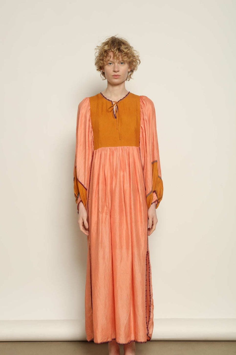 Model is wearing the Serafina Rose and Yellow Silk Dress by Supernaturae x HONS in pure handwoven silk, featuring a flowing kaftan-inspired silhouette with soft rose and golden yellow botanical-dyed tones. This sustainable artisan-made dress shows natural color variations unique to each piece, with lightweight breathable fabric and adjustable side ties, part of the House of Nomad Stories selection.