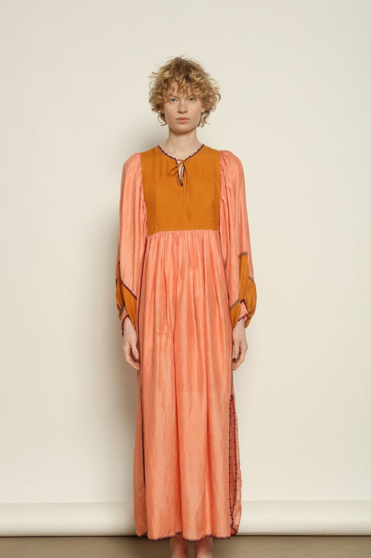 Model is wearing the Serafina Rose and Yellow Silk Dress by Supernaturae x HONS in pure handwoven silk, featuring a flowing kaftan-inspired silhouette with soft rose and golden yellow botanical-dyed tones. This sustainable artisan-made dress shows natural color variations unique to each piece, with lightweight breathable fabric and adjustable side ties, part of the House of Nomad Stories selection.