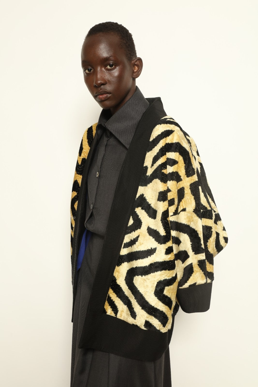 Model is wearing the Serai Ikat Velvet Jacket by Aleksandra Viktor, part of House of Woven Stories collection, handwoven Uzbek ikat velvet jacket with black collar, flowing silhouette, and vibrant blue lining