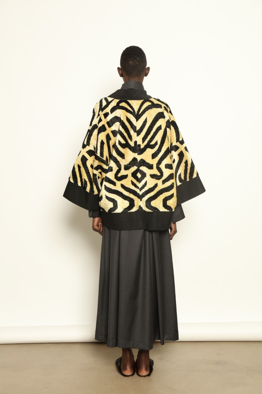 Model is wearing the Serai Ikat Velvet Jacket by Aleksandra Viktor, part of House of Woven Stories collection, handwoven Uzbek ikat velvet jacket with black collar, flowing silhouette, and vibrant blue lining