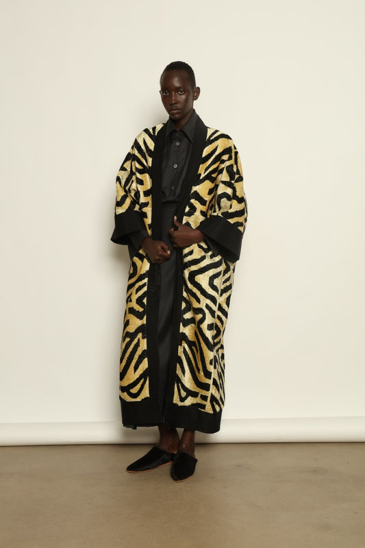 Model is wearing the Serai XL Ikat Velvet Coat by Aleksandra Viktor, part of House of Nomad Stories collection, handwoven Uzbek ikat velvet coat with bold geometric pattern, structured black collar, and cobalt lining