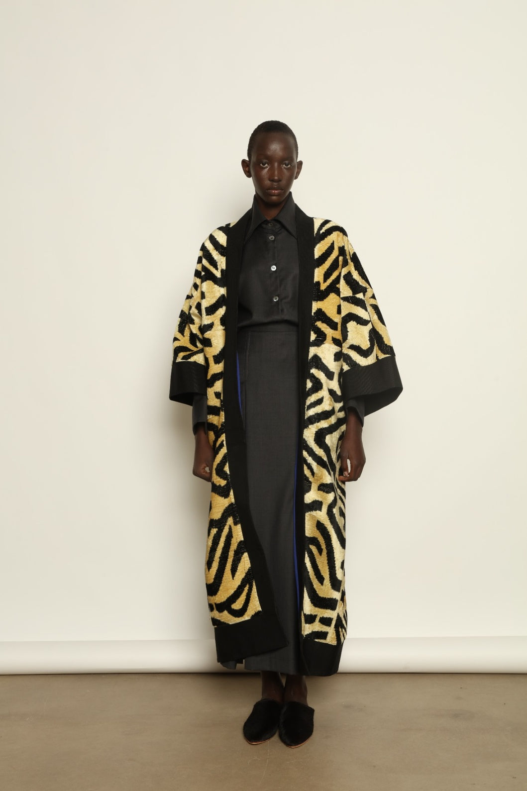 Model is wearing the Serai XL Ikat Velvet Coat by Aleksandra Viktor, part of House of Nomad Stories collection, handwoven Uzbek ikat velvet coat with bold geometric pattern, structured black collar, and cobalt lining
