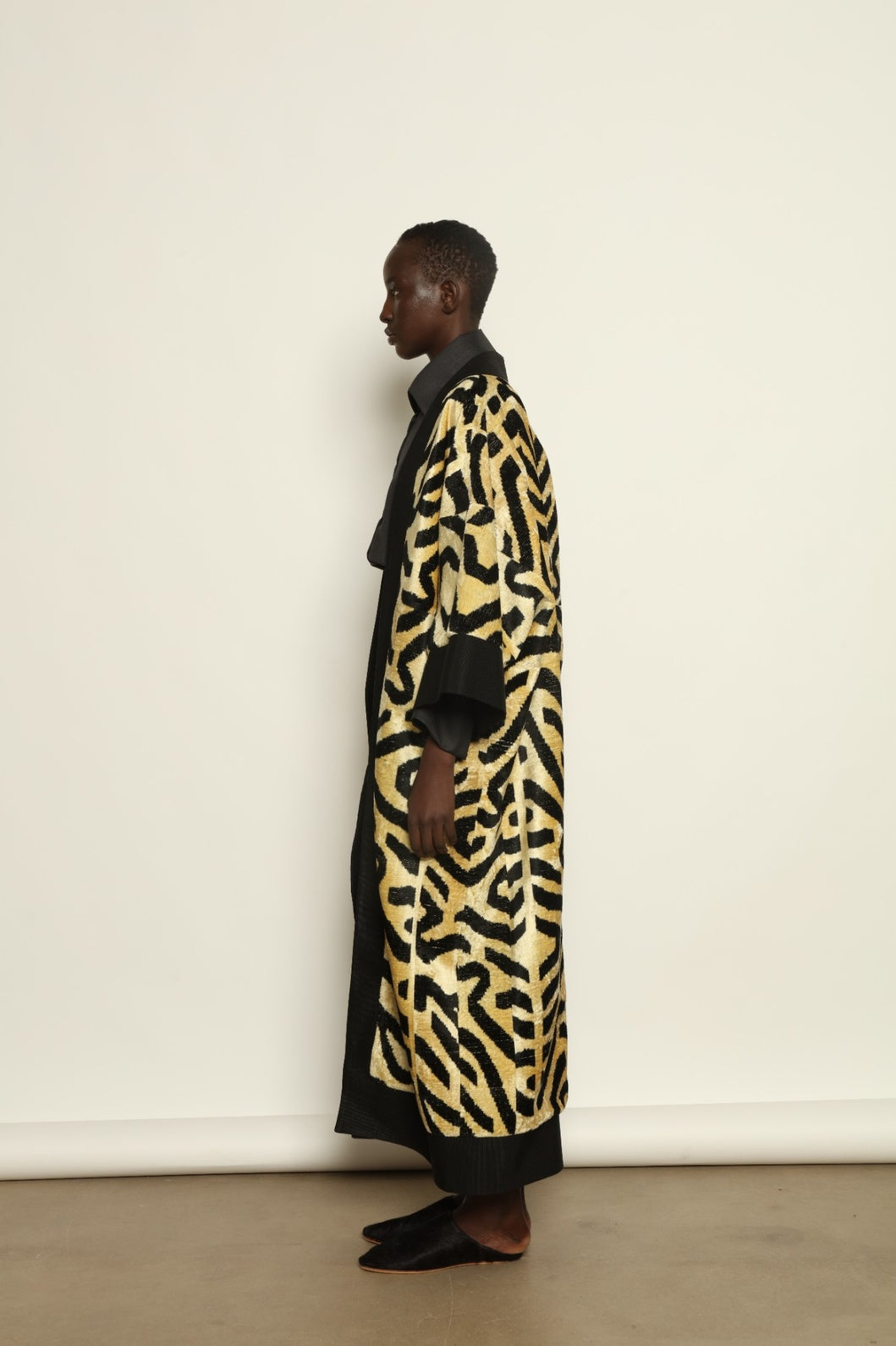 Model is wearing the Serai XL Ikat Velvet Coat by Aleksandra Viktor, part of House of Nomad Stories collection, handwoven Uzbek ikat velvet coat with bold geometric pattern, structured black collar, and cobalt lining