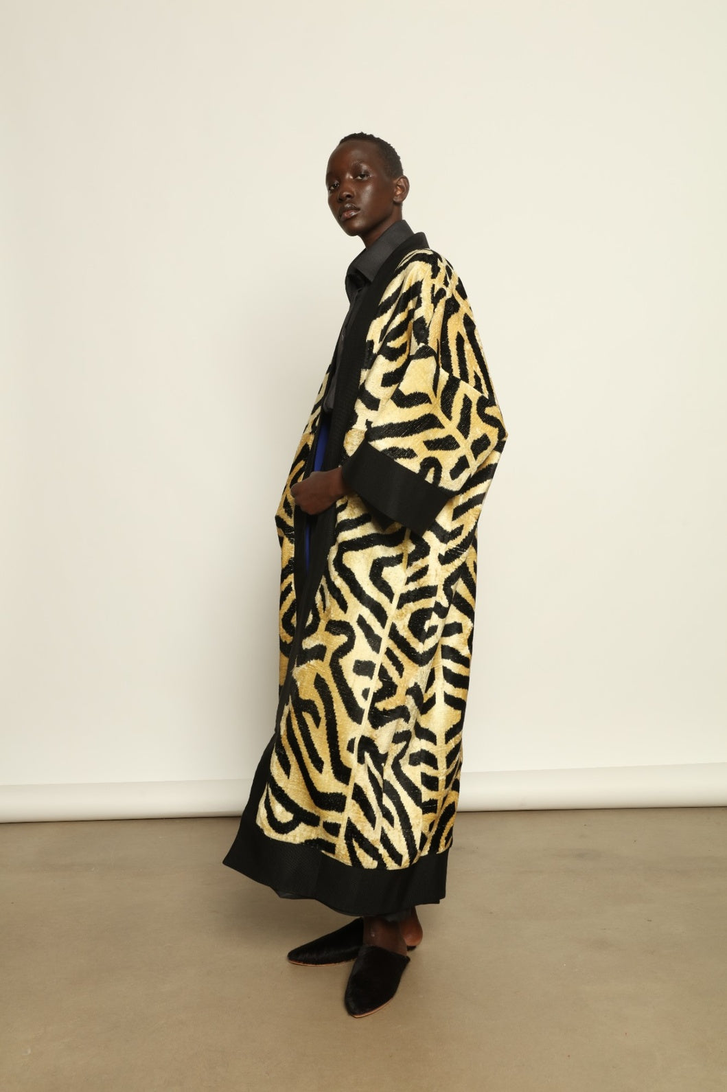 Model is wearing the Serai XL Ikat Velvet Coat by Aleksandra Viktor, part of House of Nomad Stories collection, handwoven Uzbek ikat velvet coat with bold geometric pattern, structured black collar, and cobalt lining