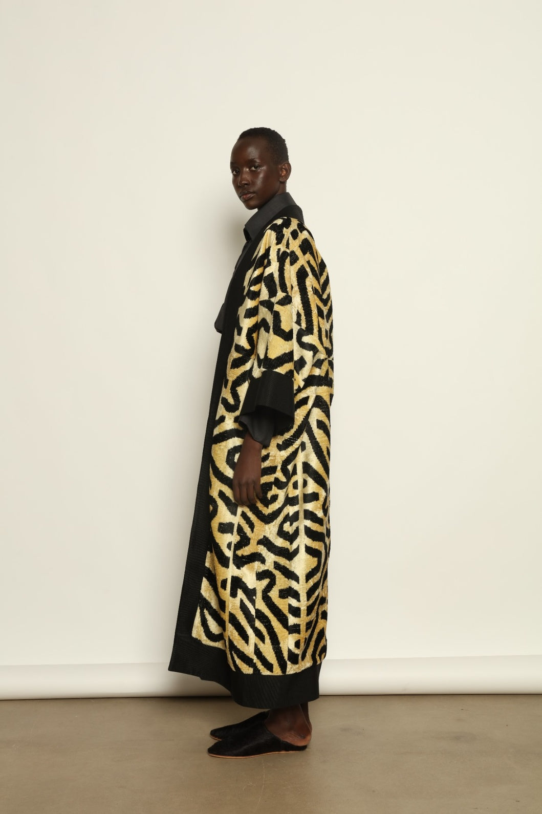 Model is wearing the Serai XL Ikat Velvet Coat by Aleksandra Viktor, part of House of Nomad Stories collection, handwoven Uzbek ikat velvet coat with bold geometric pattern, structured black collar, and cobalt lining