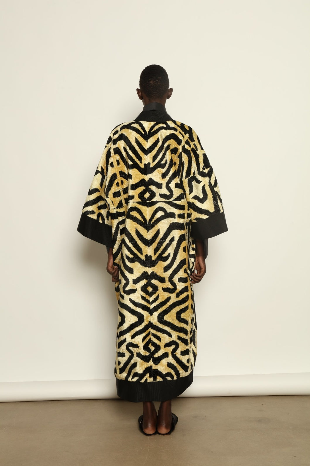 Model is wearing the Serai XL Ikat Velvet Coat by Aleksandra Viktor, part of House of Nomad Stories collection, handwoven Uzbek ikat velvet coat with bold geometric pattern, structured black collar, and cobalt lining