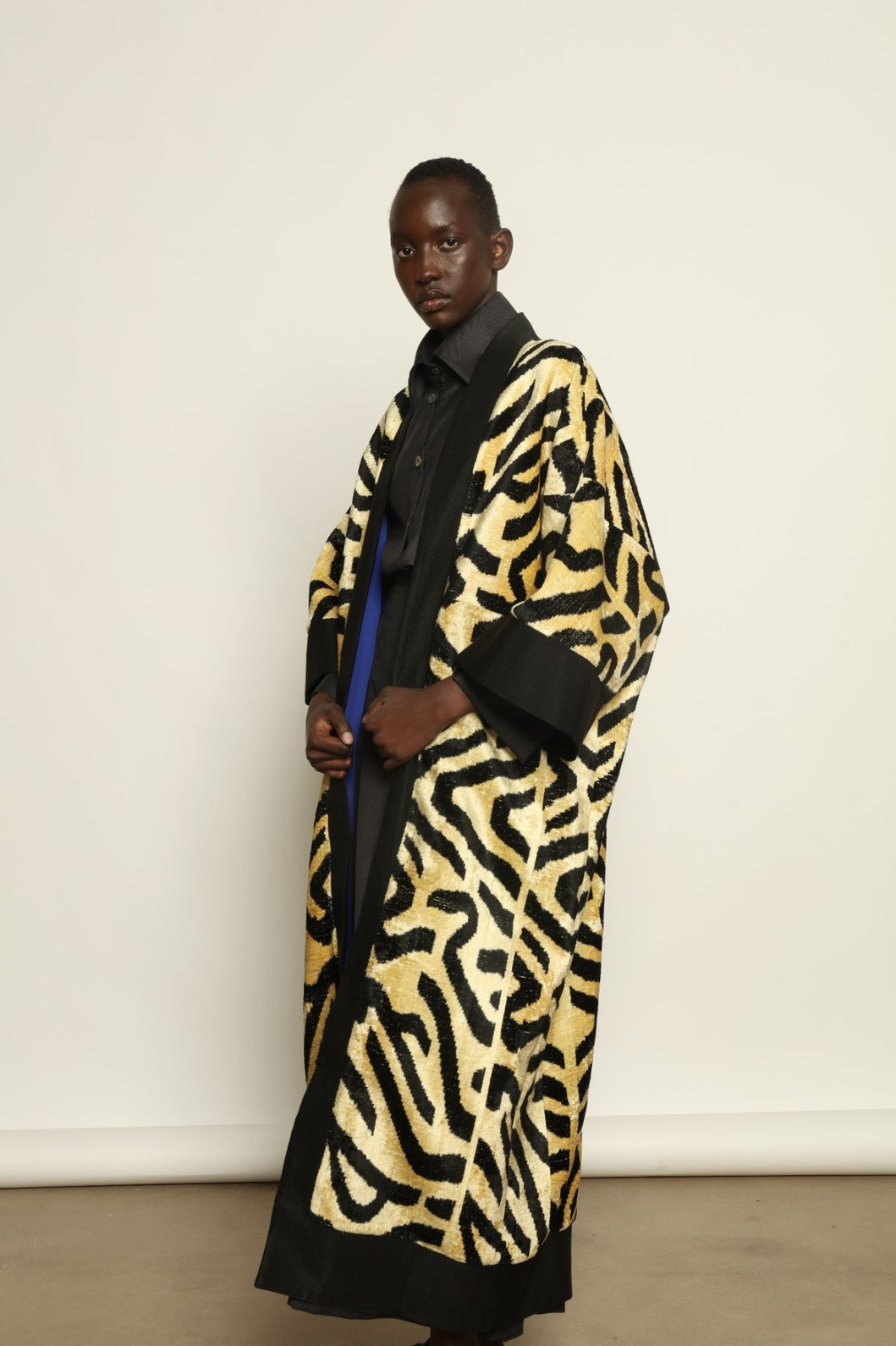 Model is wearing the Serai XL Ikat Velvet Coat by Aleksandra Viktor, part of House of Nomad Stories collection, handwoven Uzbek ikat velvet coat with bold geometric pattern, structured black collar, and cobalt lining