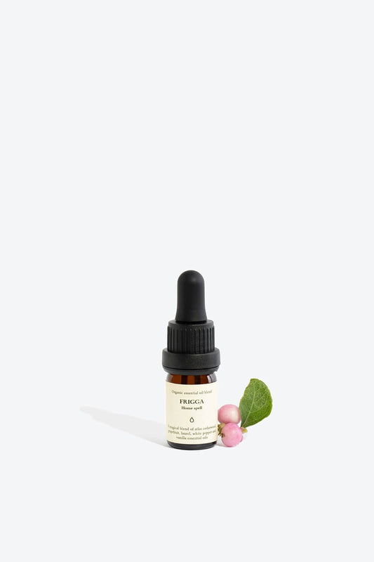 Bottle of Frigga organic essential oil blend by Smells Like Spells, placed on a natural surface with herbs, ideal for home protection and harmony rituals.