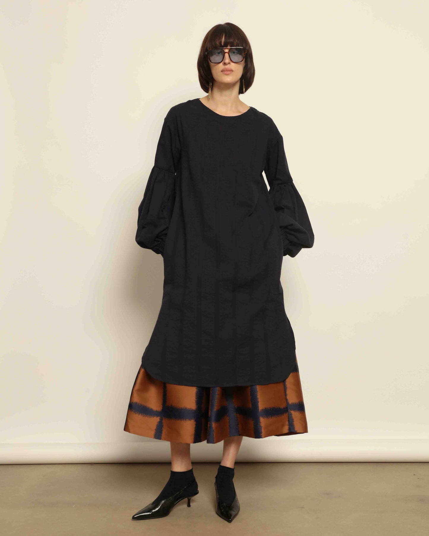 Model is wearing the Square Orange and Blue Skirt by Lunatica Milano. Pleated skirt in bronze and deep blue with striking geometric design. Feminine, elegant, and handcrafted in Italy. Part of House of Woven Stories selection.