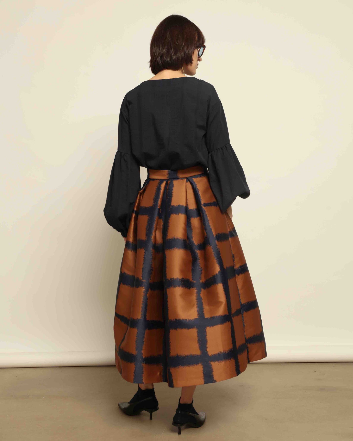 Model is wearing the Square Orange and Blue Skirt by Lunatica Milano. Pleated skirt in bronze and deep blue with striking geometric design. Feminine, elegant, and handcrafted in Italy. Part of House of Woven Stories selection.