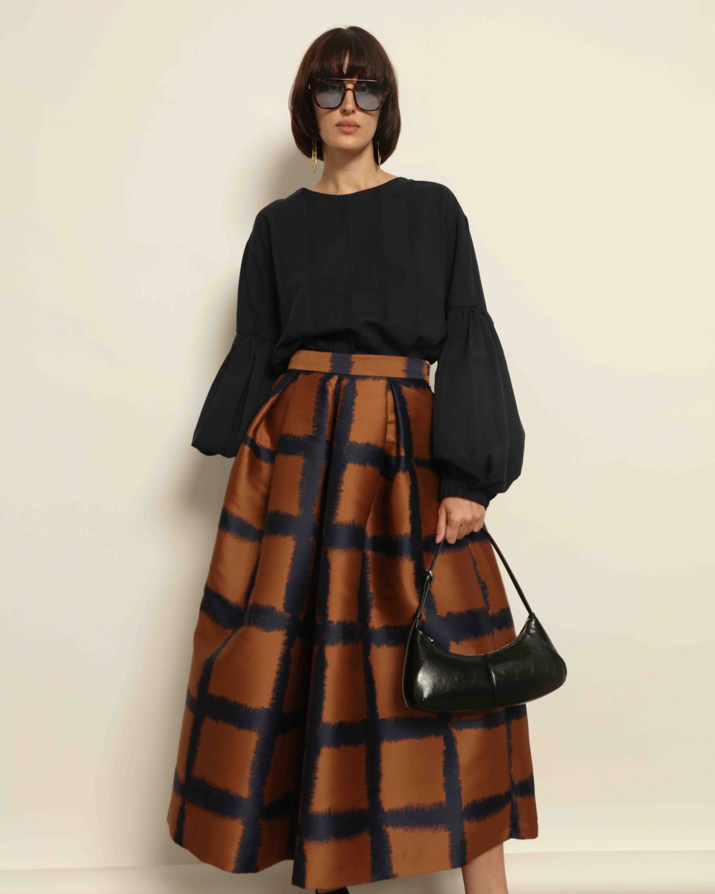 Model is wearing the Square Orange and Blue Skirt by Lunatica Milano. Pleated skirt in bronze and deep blue with striking geometric design. Feminine, elegant, and handcrafted in Italy. Part of House of Woven Stories selection.