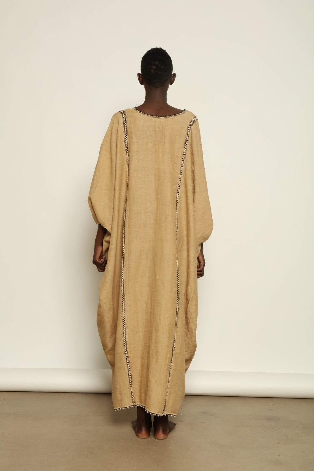 Model is wearing the Thea Beige Linen Dress by Supernaturae x HONS in soft botanical sandy beige linen, featuring a relaxed flowing silhouette, structured breathable fabric and elegant open back design. Part of the House of Woven Stories selection, this ethical slow fashion piece is hand-dyed with natural pigments, showing organic tonal variations.