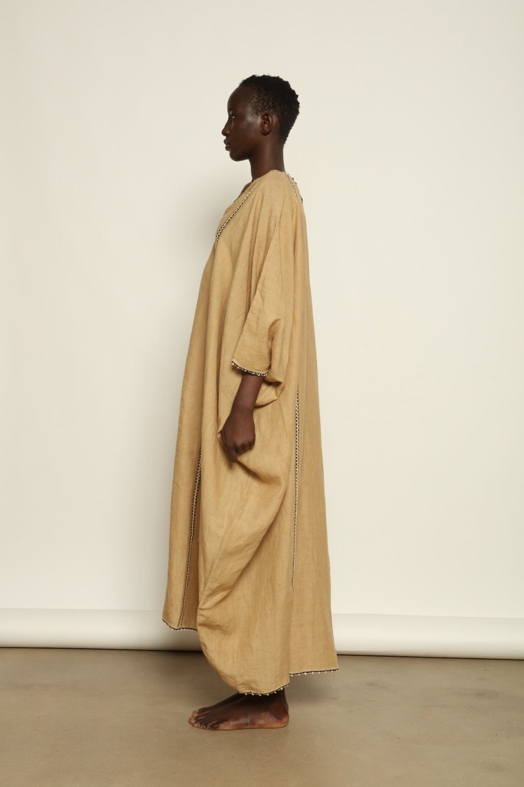 Model is wearing the Thea Beige Linen Dress by Supernaturae x HONS in soft botanical sandy beige linen, featuring a relaxed flowing silhouette, structured breathable fabric and elegant open back design. Part of the House of Woven Stories selection, this ethical slow fashion piece is hand-dyed with natural pigments, showing organic tonal variations.