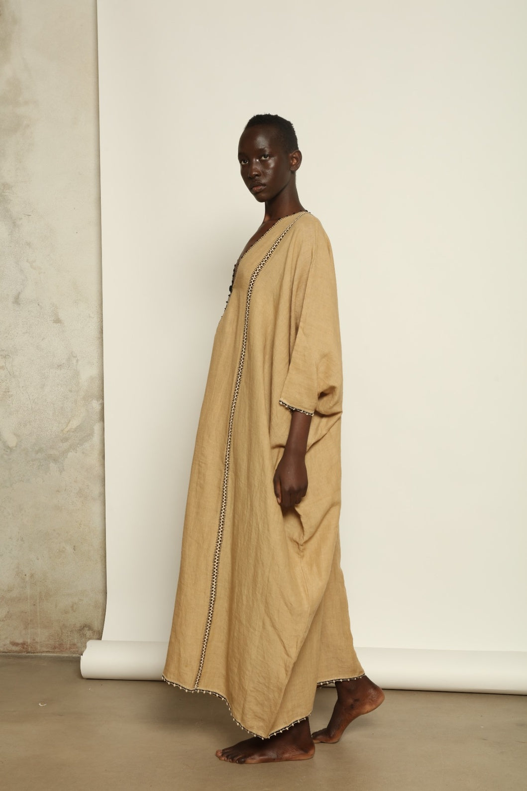 Model is wearing the Thea Beige Linen Dress by Supernaturae x HONS in soft botanical sandy beige linen, featuring a relaxed flowing silhouette, structured breathable fabric and elegant open back design. Part of the House of Woven Stories selection, this ethical slow fashion piece is hand-dyed with natural pigments, showing organic tonal variations.
