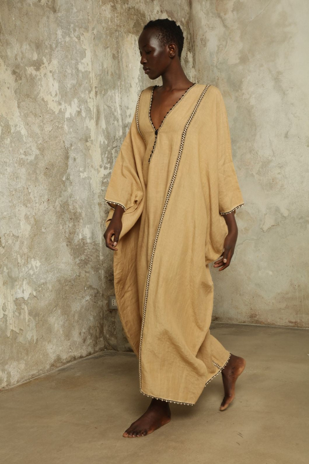 Model is wearing the Thea Beige Linen Dress by Supernaturae x HONS in soft botanical sandy beige linen, featuring a relaxed flowing silhouette, structured breathable fabric and elegant open back design. Part of the House of Woven Stories selection, this ethical slow fashion piece is hand-dyed with natural pigments, showing organic tonal variations.