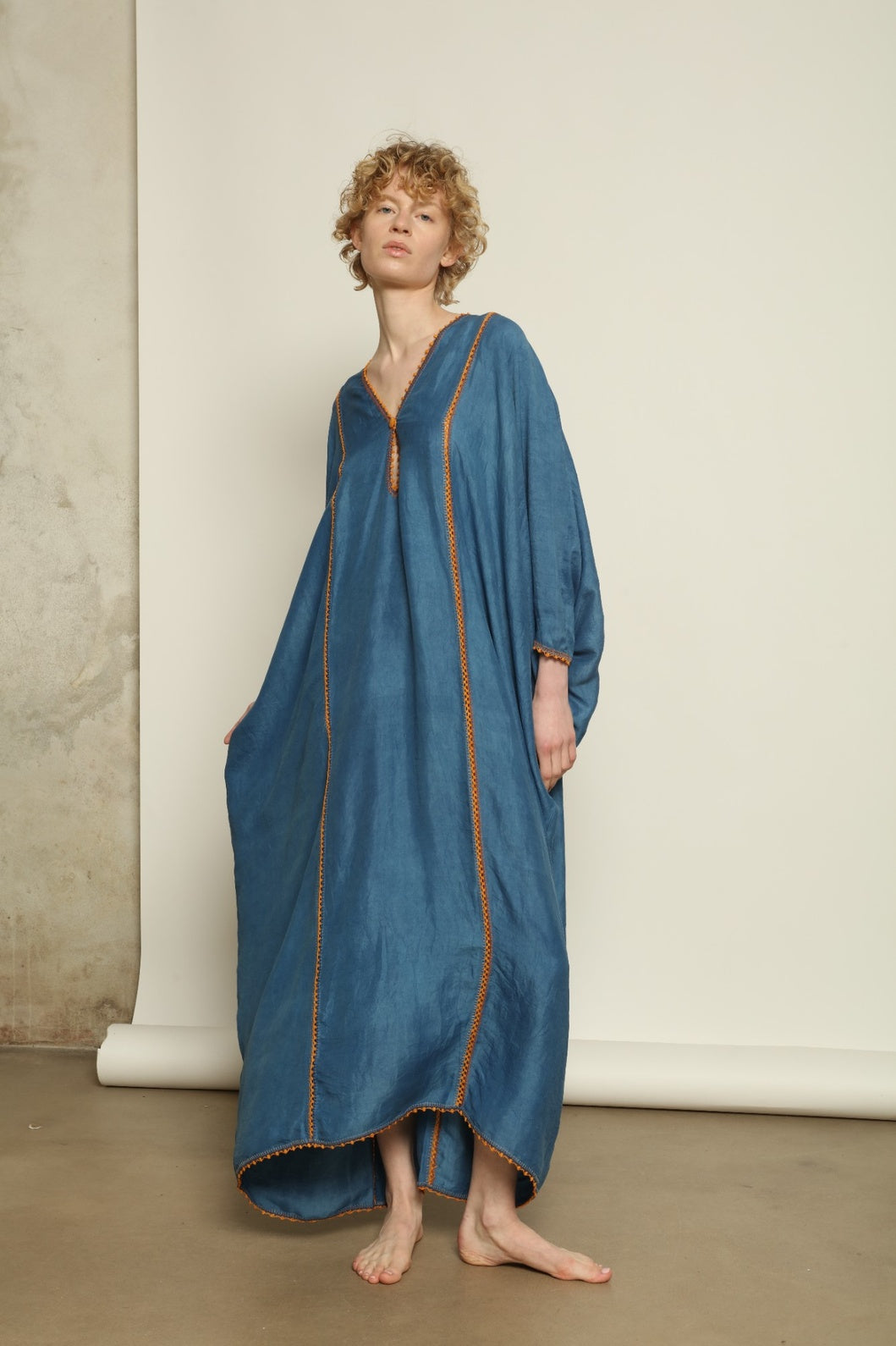 Model is wearing the Thea Blue Silk Dress by Supernaturae x HONS in deep indigo botanical-dyed silk chiffon, featuring a fluid ethereal silhouette and delicate hand-crochet edges. This sustainable slow luxury dress shows natural pigment variations that make each piece unique, crafted in small-batch production in Mexico using ancestral techniques. Part of the House of Woven Stories selection.