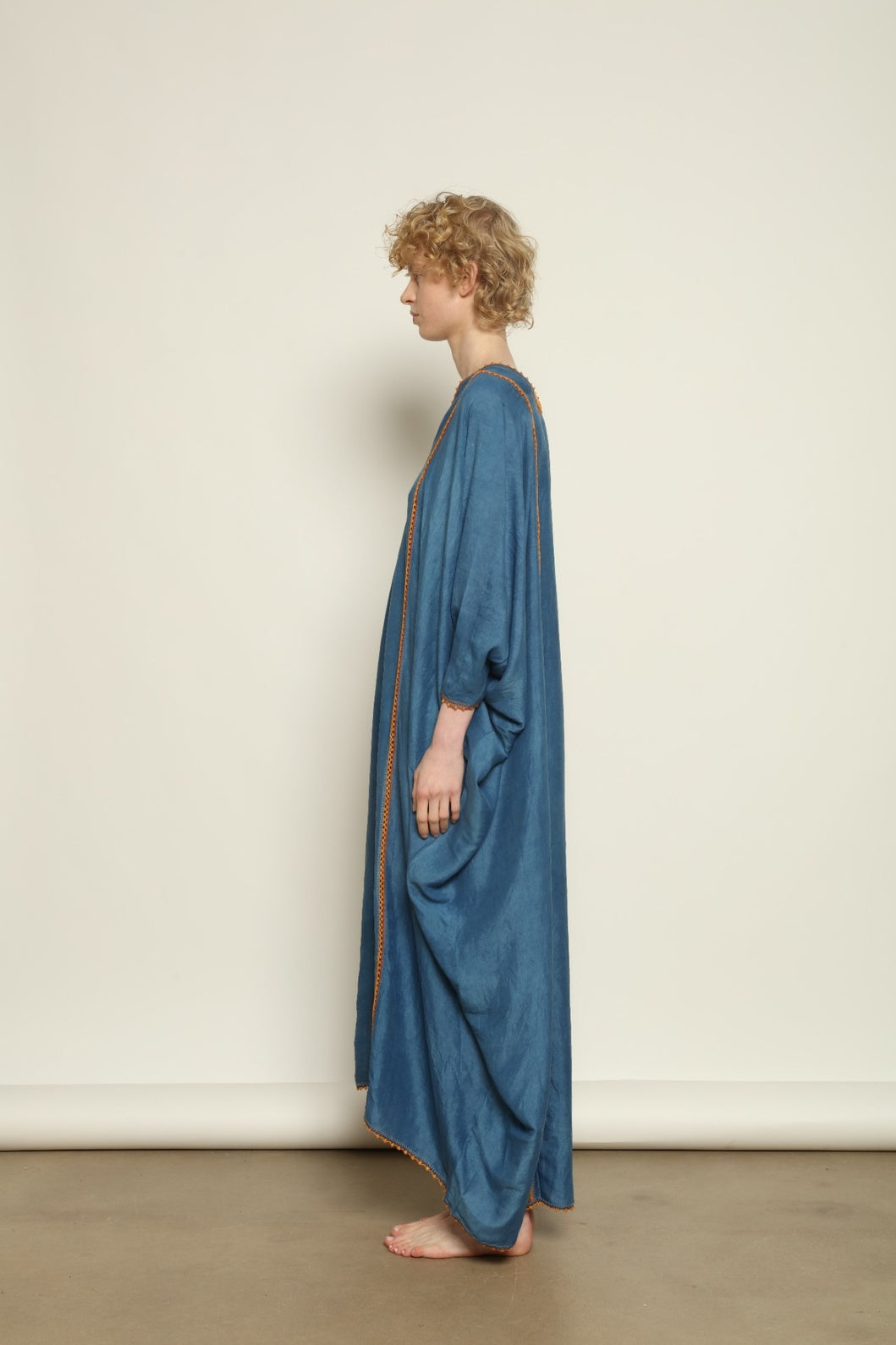 Model is wearing the Thea Blue Silk Dress by Supernaturae x HONS in deep indigo botanical-dyed silk chiffon, featuring a fluid ethereal silhouette and delicate hand-crochet edges. This sustainable slow luxury dress shows natural pigment variations that make each piece unique, crafted in small-batch production in Mexico using ancestral techniques. Part of the House of Woven Stories selection.