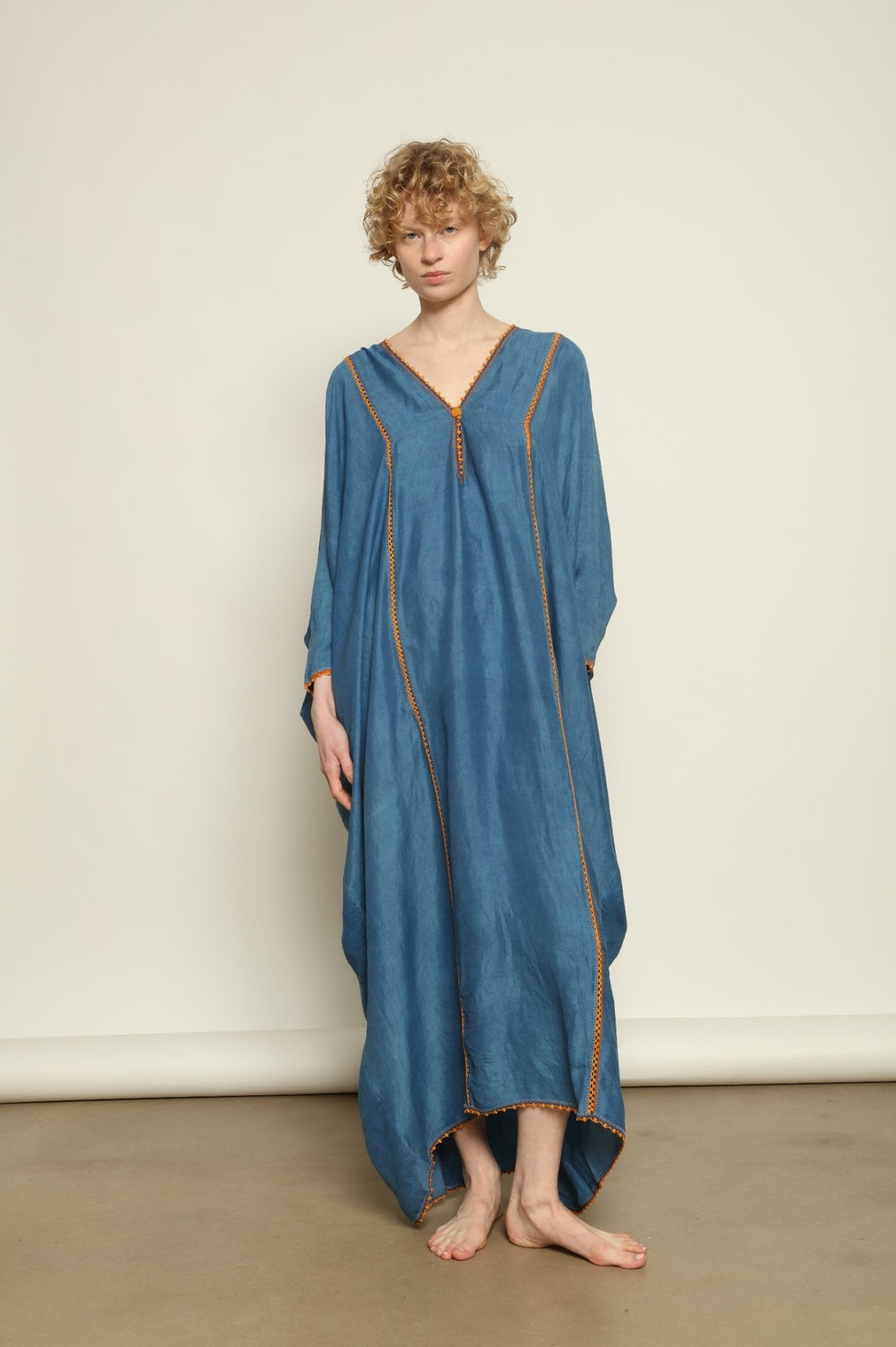 Model is wearing the Thea Blue Silk Dress by Supernaturae x HONS in deep indigo botanical-dyed silk chiffon, featuring a fluid ethereal silhouette and delicate hand-crochet edges. This sustainable slow luxury dress shows natural pigment variations that make each piece unique, crafted in small-batch production in Mexico using ancestral techniques. Part of the House of Woven Stories selection.