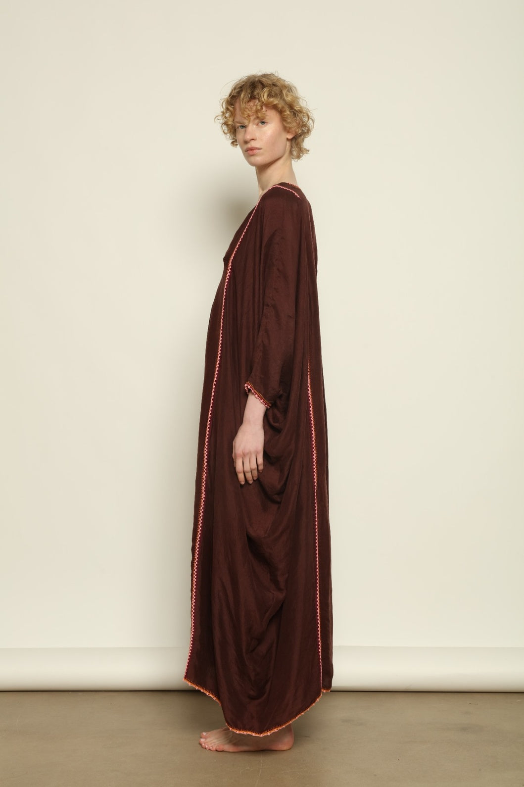 Model is wearing the Thea Brown Silk Dress by Supernaturae x HONS in rich earthy brown handwoven silk from Murshidabad, featuring a soft open back and flowing silhouette. Botanical dyed with natural pigments, this sustainable slow luxury dress shows subtle tonal variations and artisanal craftsmanship, part of the House of Woven Stories selection